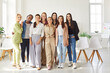 © Studio Romantic - Full length portrait of happy smiling young diverse female company employees wearing casual clothes standing in modern office and looking cheerful at camera. Teamwork and business concept.