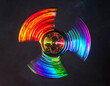 © Thanatchaphan - Rainbow holographic fidget spinner with glossy finish and vibrant colors spinning against dark background, creating eye catching light trails