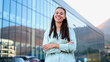 © PeopleVideos - Confident businesswoman smiling with crossed arms in front of a modern office building, showcasing leadership and success in the corporate world