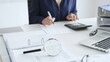 © rogerphoto - Close up of magnifying glass and calculator over financial documents opposite female accountant analyzing data, reviewing reports, binders and laptop on a white desk. Audit and taxes concept