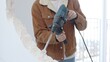 © rogerphoto - Unrecognizable construction worker demolishing concrete wall with rotary hammer, wearing protective safety gear. Renovation concept, closeup vertical view
