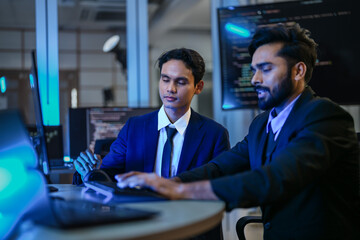 diverse AI developers collaborate in a late-night coding session. A senior engineer mentors his colleague as they program a complex machine learning algorithm together.