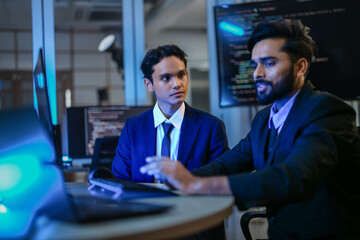 diverse AI developers collaborate in a late-night coding session. A senior engineer mentors his colleague as they program a complex machine learning algorithm together.