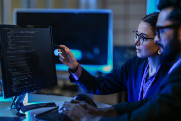 diverse AI developers collaborate in a late-night coding session. A senior engineer mentors his colleague as they program a complex machine learning algorithm together.