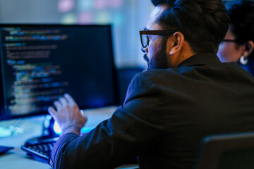 A backend AI developer programs a complex algorithm late at night in a data center. A focused engineer architecting a new machine learning system for data analysis or cybersecurity.