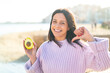 © luismolinero - Young woman at outdoors holding an avocado at outdoors proud and self-satisfied