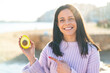 © luismolinero - Young woman at outdoors holding an avocado at outdoors and pointing it