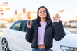 © luismolinero - Young woman at outdoors holding car keys at outdoors saluting with hand with happy expression