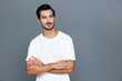 © SHOTPRIME STUDIO - Smiling man with crossed arms looking confidently at the camera, dressed in a casual white t-shirt, captured against a soft gray background. Lifestyle concept.