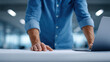 © Nakarin - Man in blue shirt leaning over table with laptop and documents, focused on work in modern office environment