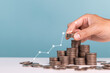 © sichon - Invest,Investment,profit,saving money and planning businesses. Man holds coin in his hand with coins stack and upward arrows Indicating profit and growing