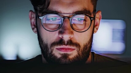 Man wearing glasses focused on a computer screen at night