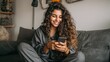 © Johannes - happy millennial hispanic teen girl checking social media holding smartphone at home smiling young latin woman using mobile phone app playing game shopping online ordering delivery relax on sofa no l