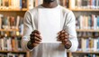 © Nan_Stock - Man presents book cover in library, perfect for education, literature, or design mockups with space for text