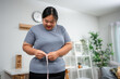 © Kawee - Asian young overweight woman measuring waist with tape measure at home.