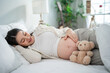 © Kawee - Asian young pregnant woman gently stroking belly while lying down on bed.