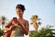 © we.bond.creations - Young woman enjoying summer holidays in a tropical paradise, using her smartphone to connect and share moments under sunny skies