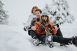 © qunica.com - Group of friends sledding down a snow-covered hill, smiling and having fun during a beautiful winter day surrounded by snowy trees and enjoying outdoor holiday activities.