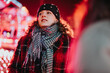 © qunica.com - A fashionable woman stands outdoors during a vibrant winter evening, surrounded by bright festive lights, enjoying the atmosphere of the holiday season.