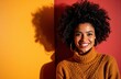 © starush - A smiling woman with natural curly hair wearing a mustard sweater against a warm red background