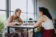 © qunica.com - Two women are sharing a focused discussion while seated at a table in a sunlit cafe, enjoying beverages and snacks. The setting exudes connection, relaxation, and an atmosphere of communication.