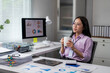 © Apichat - woman is sitting at a desk with a computer monitor and a cup of coffee