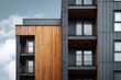 © Marina Demidiuk - Building facade with black and brown cladding. Dark grey metal cladding with wood panels finish on apartment block. Bottom view. Blue sky. Timber paneling on modern architectural design urban setting