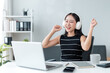 © amnaj - Young asian businesswoman wearing headphones celebrating success while working from home office