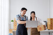 © amnaj - Two cheerful asian colleagues managing online orders on a laptop while working together in a warehouse full of cardboard boxes