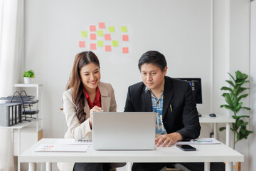 Wall Mural - two asian businesspeople working together in the office, analyzing financial charts and using laptop