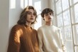 © hkjdesign - A young man and woman in knit sweaters pose near a sunlit window.