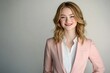 © hkjdesign - A young woman with blonde wavy hair smiles confidently while wearing a pink blazer and white shirt.