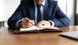 © Zyariss - Professional Person in Suit Writing Notes in a Notebook on a Wooden Desk
