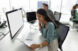 © fizkes - Young Latina woman deeply focused on reviewing important document, agreement or contract seated at table with modern computer with white blank mock up monitor, working in contemporary coworking office