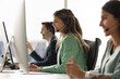 © fizkes - Group of customer service representatives sit at modern office workstation, focus on young Hispanic woman wearing headset engaged in conversation, assisting client or participating in virtual meeting