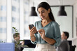 © fizkes - Young 30s female employee using smartphone in workplace, checking messages, reading emails or reviewing business-related information, staying connected during workday, engaged in digital communication