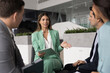 © fizkes - Young Latina businesswoman speaking confidently to group of three colleagues during briefing in office, leading conversation or presenting new idea, engaged in project presentation and brainstorming