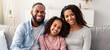 © Prostock-studio - Happy Family. Portrait of cheerful African American daughter sitting on the couch between her smiling parents. Positive woman, man and girl posing for photo and looking at camera at home