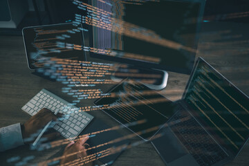 Coding and software development concept, with programmer typing on keyboard surrounded by laptop, tablet, and monitor showing glowing source code lines.