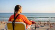 © An - A lifeguard in an orange shirt sits on a yellow chair on a crowded beach, observing the ocean.