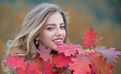 Wall Mural - Autumn face of happy young woman. Smiling girl on autumn fall background. Beauty girl with fall leaves. Autumn model with fall leaf. Autumn portrait of happy girl.