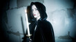 © Olga B.G. - Non-binary person in black velvet cloak holding a candle in dim light