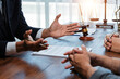 © amnaj - Lawyer is gesturing with hands while explaining contract details to client during meeting in law firm with gavel and balance scale in background