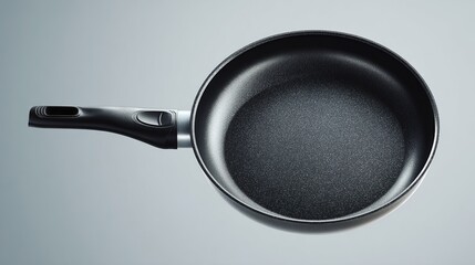 Black non-stick frying pan with a plastic handle against a plain grey background