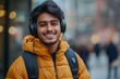 © Arvind - Happy young Indian man listens to music or a podcast on his phone while standing outside with headphones, smiling, Generative AI