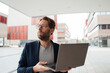 © Westend61 - Thoughtful businessman holding laptop outside building