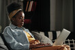 © TrueFrame Collective - Modern young African American woman sitting relaxed on sofa at home working on laptop, horizontal medium portrait