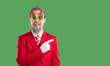 © Studio Romantic - Happy man in Christmas party costume showing something on copy space side. Bearded man wearing red suit, tie and funny Xmas glasses standing isolated on green color background and pointing sideways