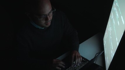 Male programmer works late at night with green code reflecting on his lenses, focusing on software development, coding, and cybersecurity analysis in dark room. 
