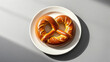 © Bonsales - Golden brown pretzel sits on a white plate, illuminated by natural light, creating a visually appealing image for food and bakery related projects